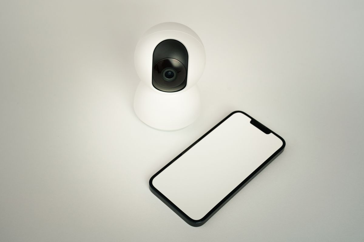Telecamera IP di sorveglianza domestica accanto a smartphone con app dedicata di controllo remoto