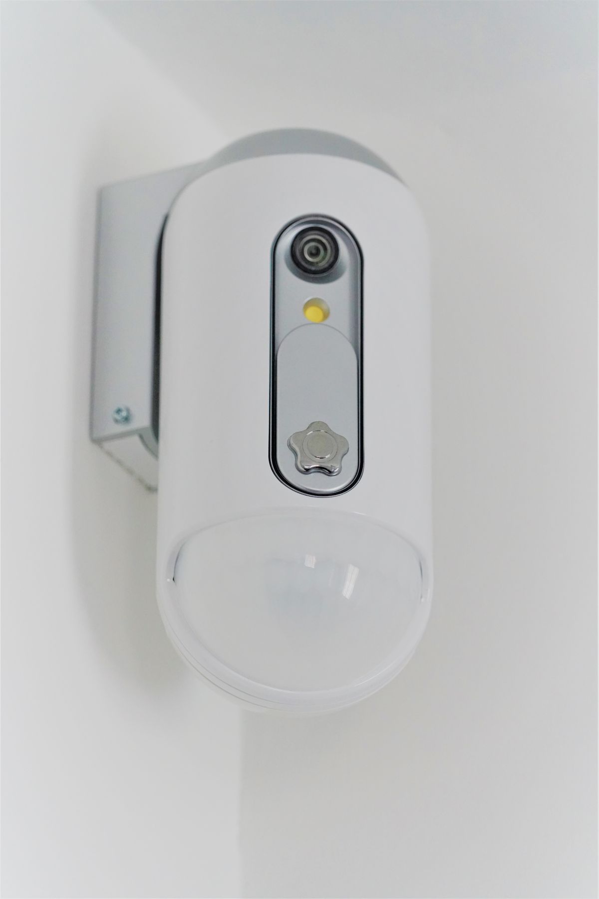 Sensore volumetrico PIR con telecamera integrata, fissato a parete bianca in ambiente residenziale