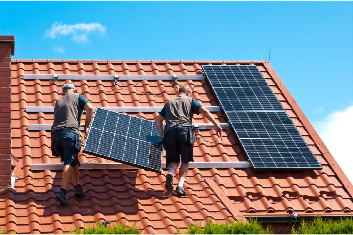 Due installatori montano pannelli fotovoltaici monocristallini su tetto a coppi esposto sud: impianto residenziale con telai in alluminio anodizzato