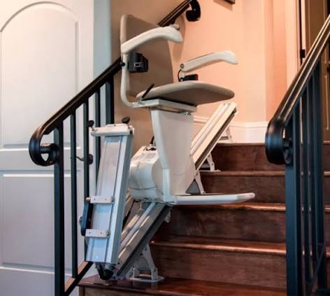 Poltroncina del montascale con seduta imbottita avorio, braccioli ergonomici, pedana poggiapiedi ribaltabile abbassata, telecomando sul bracciolo destro