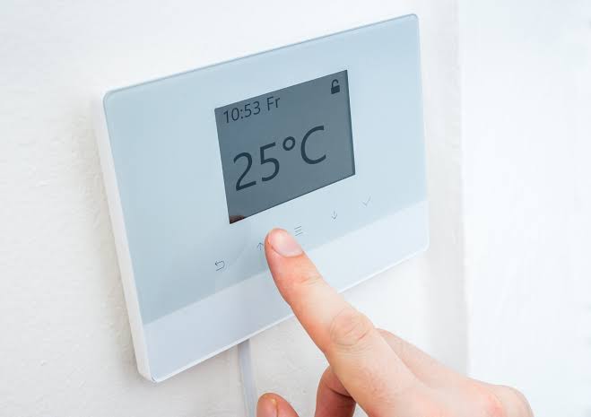 Termostato a parete con display digitale che mostra 25°C, regolato con il dito: controllo intelligente della pompa di calore